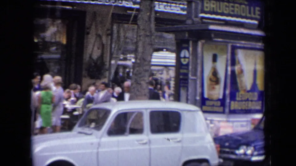 1963 France cafe street scene with a visible Brugerolle liquor advertisement, pedestrians, outdoor seating, and a white vintage car.