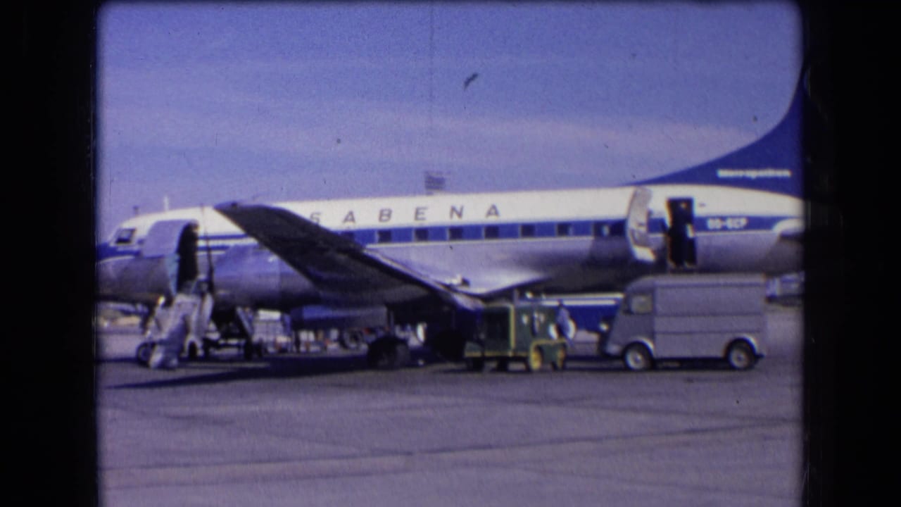1963 France 8mm frame showing a Sabena aircraft parked on the tarmac with its door open, stairs deployed, and ground vehicles nearby.