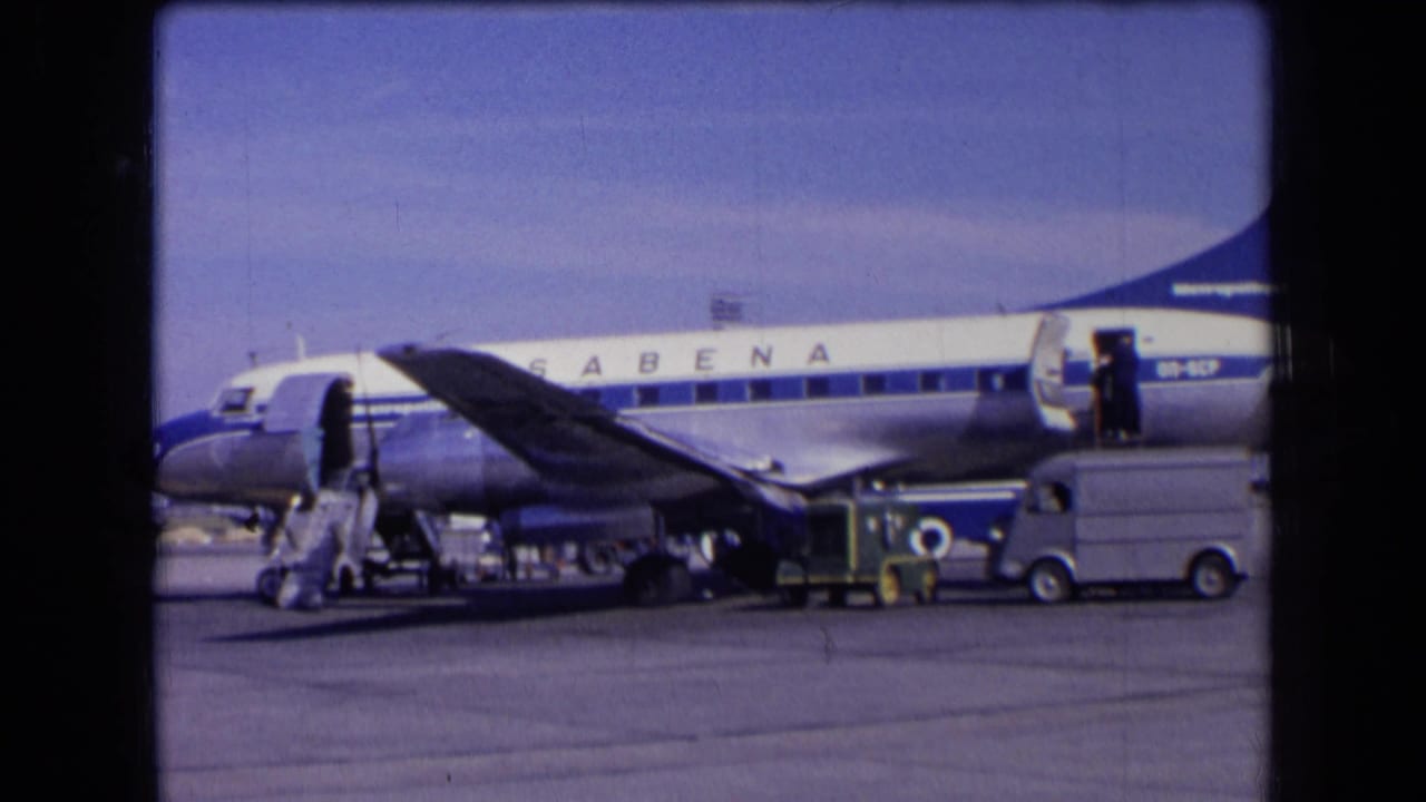 1963 France frame of a blue and white Sabena airliner beside baggage handling equipment and a small service vehicle on the airport ramp.