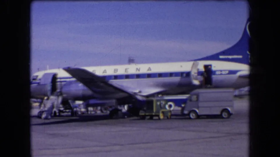 1963 France 8mm still showing Sabena airport ramp activity with baggage handling gear, crew, stairs, and a service van near the aircraft.