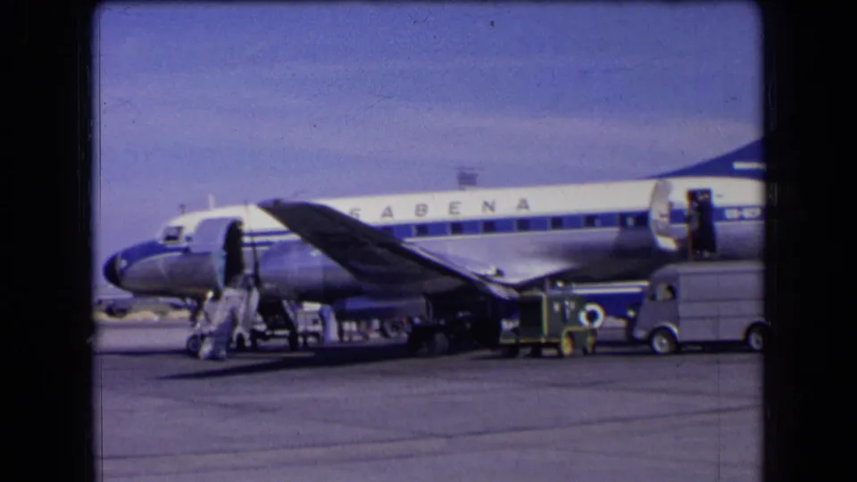 A Sabena commercial aircraft appears parked on a French airport tarmac in 1963 with support vehicles and people visible.