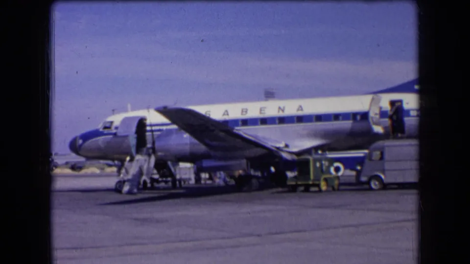 1963 France home-movie frame of a Sabena airliner during airport ground operations, with stairs and vehicles in view.