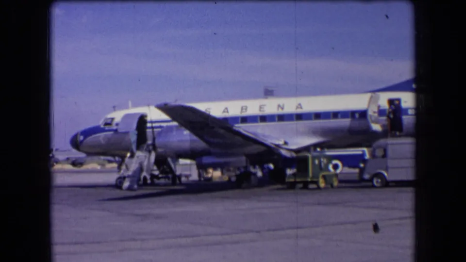 A 1963 France tarmac view shows the Sabena aircraft, deployed stairs, service vehicles, and visible people in 8mm color footage.