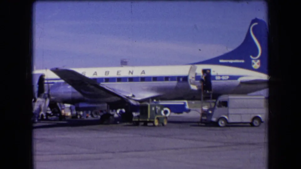 1963 France airport view of a Sabena airplane in blue and white livery with service vehicles and people beside the stairs.