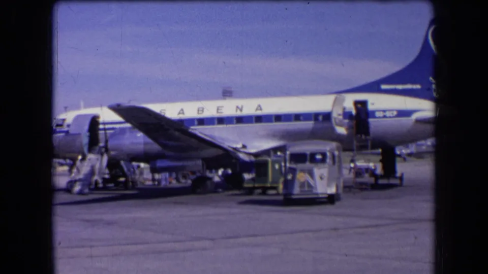 1963 France home-movie frame showing a small service van crossing the tarmac in front of a Sabena airliner during boarding preparations.
