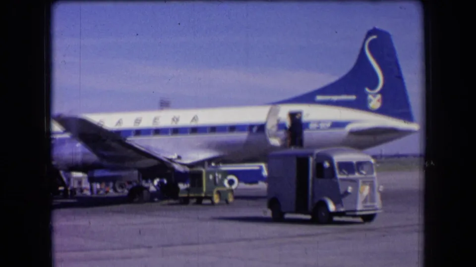 1963 France airport view of a blue-and-white Sabena jet with ground vehicles and an open aircraft door on the tarmac.