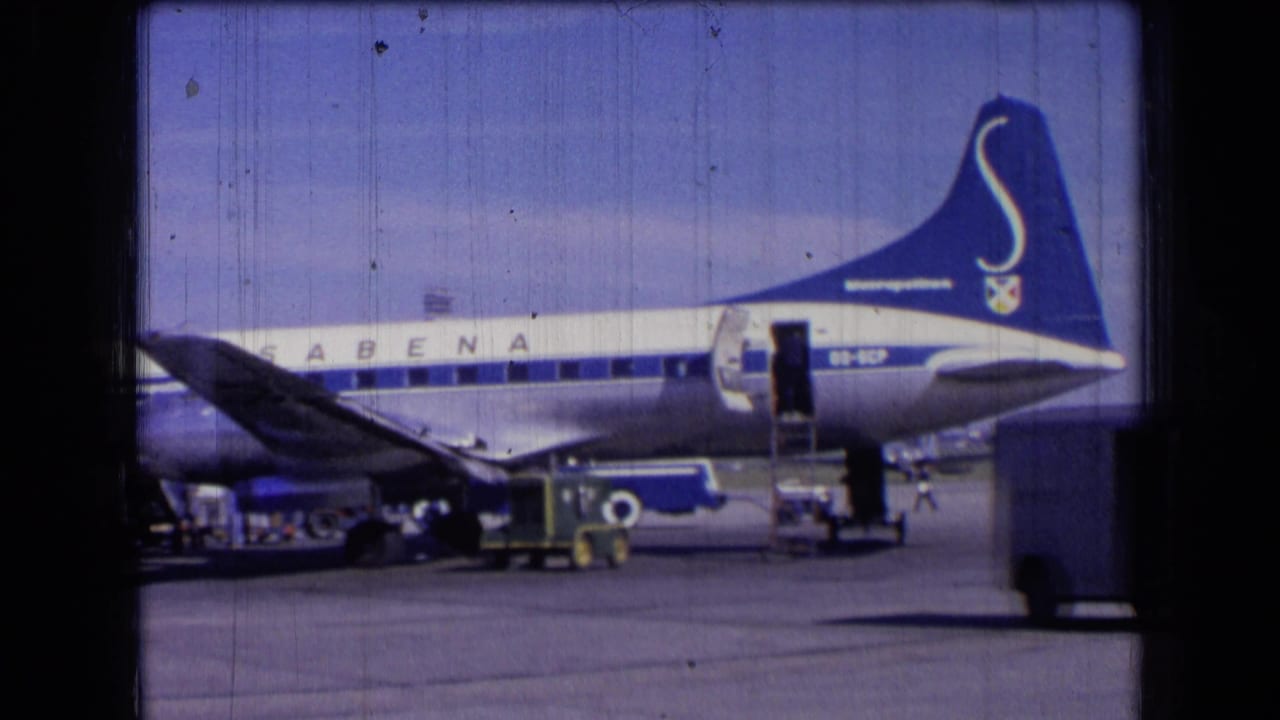 Blue-and-white Sabena jet in France, 1963, seen from the side with an open door and luggage handling equipment below.