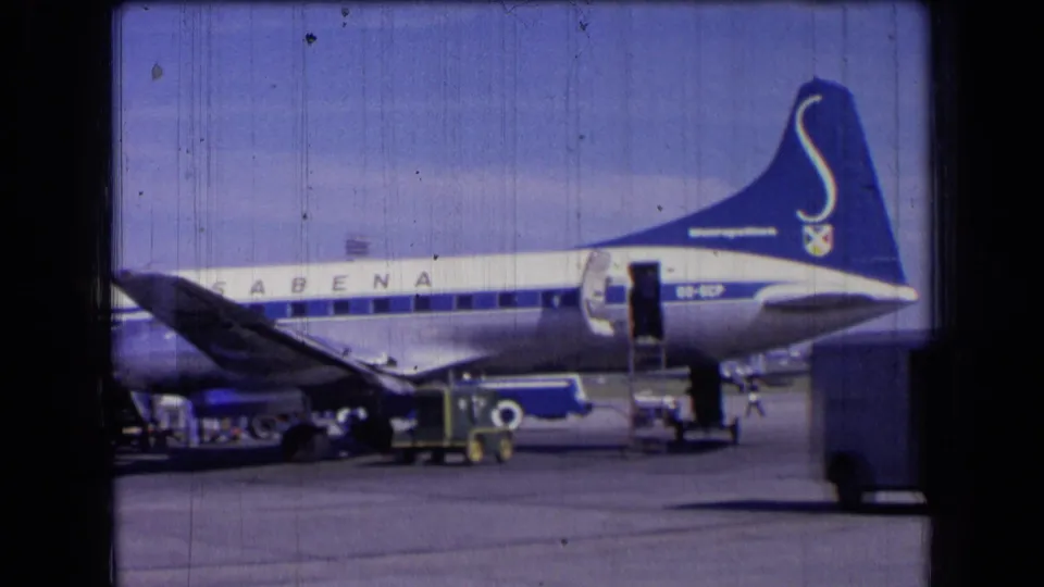 Blue-and-white Sabena jet in France, 1963, seen from the side with an open door and luggage handling equipment below.