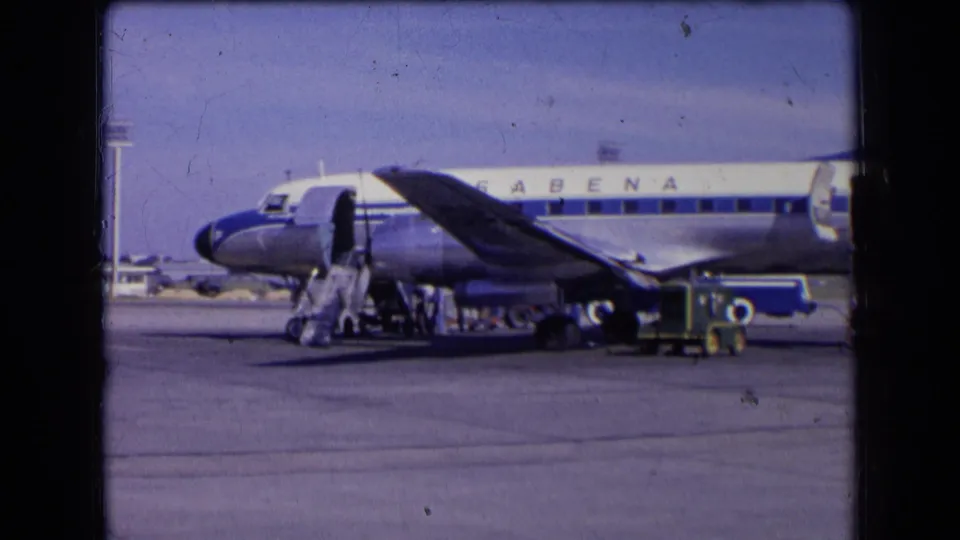 Front portion of a Sabena jet at a French airport in 1963, with portable stairs and ground crew near baggage carts.