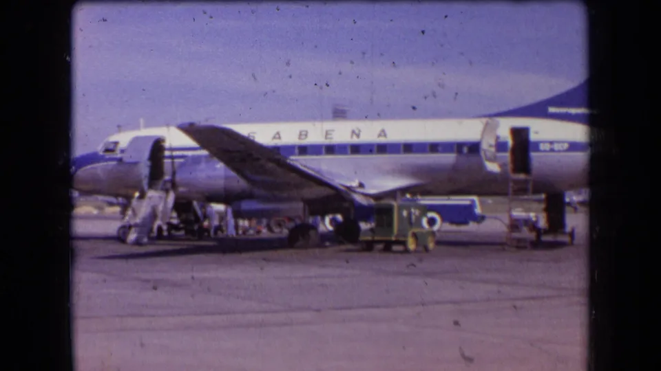1963 France frame of a Sabena passenger plane on the apron, with open door, stairs, service vehicles, and distant workers near the fuselage.