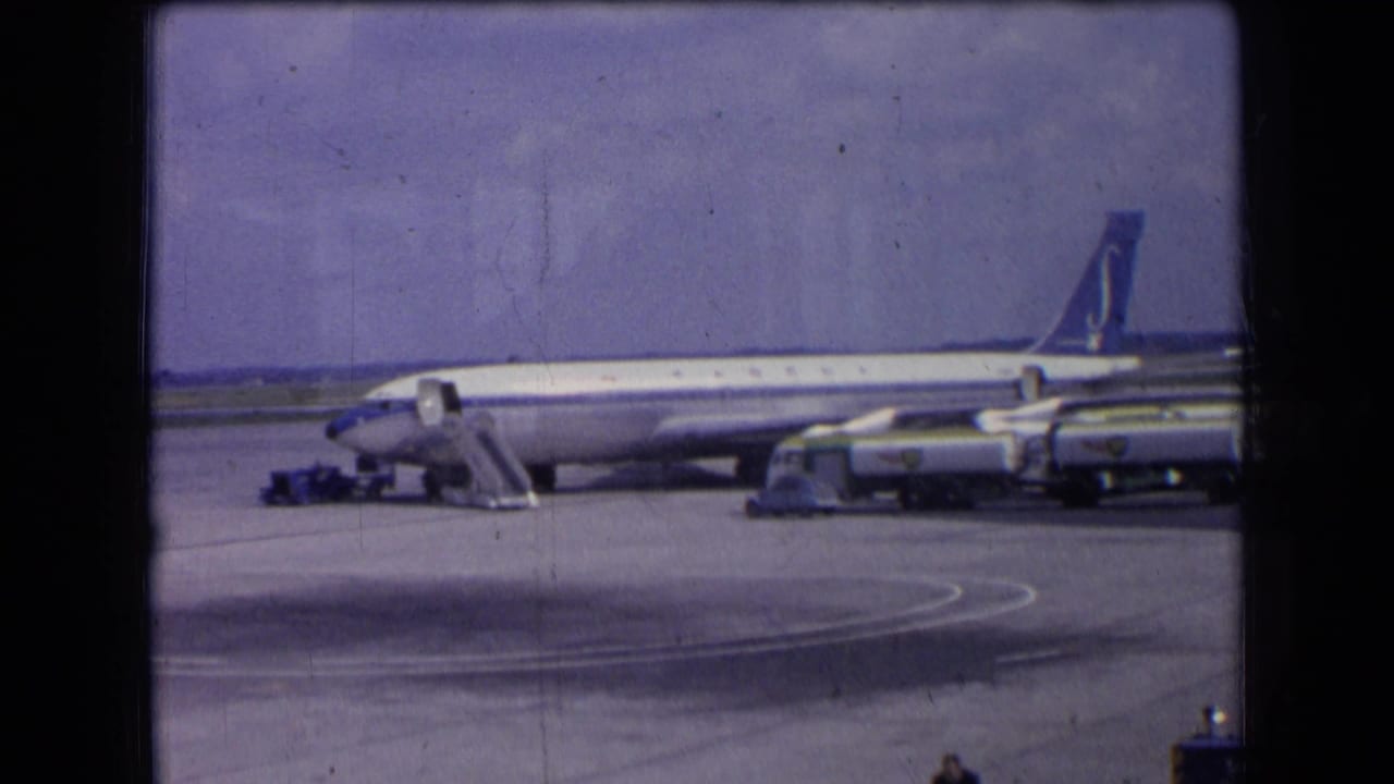 1963 France 8mm frame of a Sabena aircraft on the apron, with service vehicles aligned near the fuselage and tail visible against the sky.