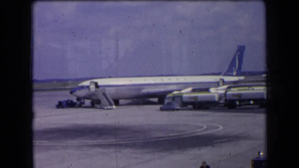 1963 France 8mm frame of a Sabena aircraft on the apron, with service vehicles aligned near the fuselage and tail visible against the sky.