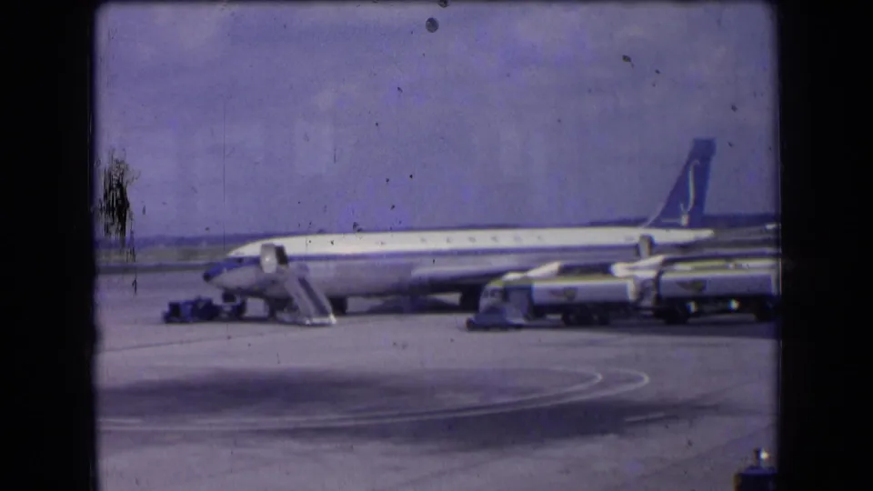 1963 France home-movie frame showing the Sabena jet from a similar tarmac angle, with stairs, vehicles, and open apron space visible.