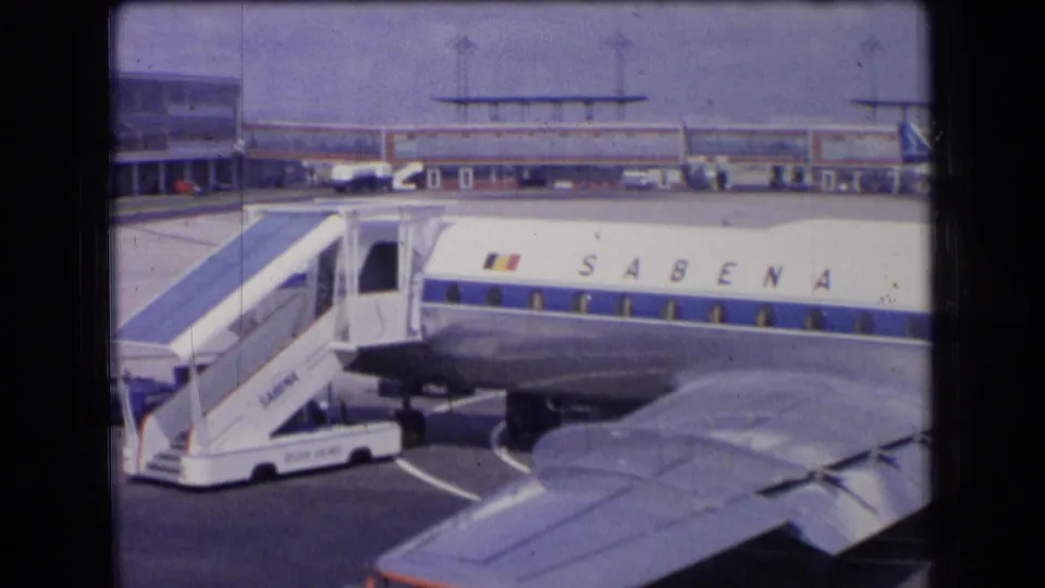 1963 France 8mm frame showing the Sabena fuselage and Belgian flag marking beside mobile stairs, with terminal structures and an aircraft wing in view.