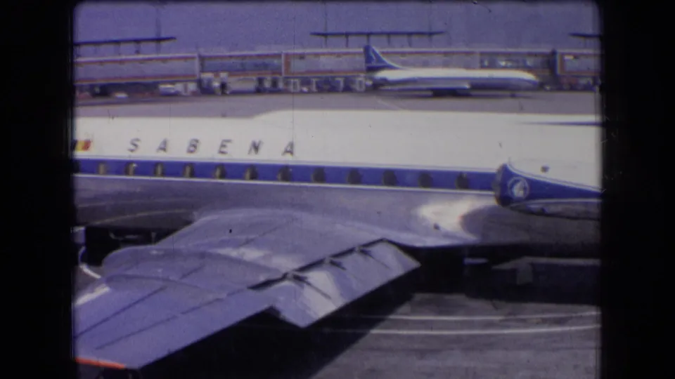 1963 France frame with a Sabena aircraft parked near terminal buildings, wing in foreground, and another airplane in the background.
