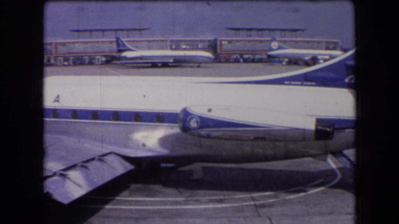 Sabena aircraft body and wing fill the foreground at a French airport, with parked planes and terminal buildings in the background.