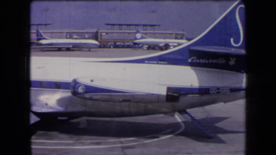 The blue tail of a Sabena Caravelle appears beside the wing and engine, with other aircraft and terminal structures behind it.