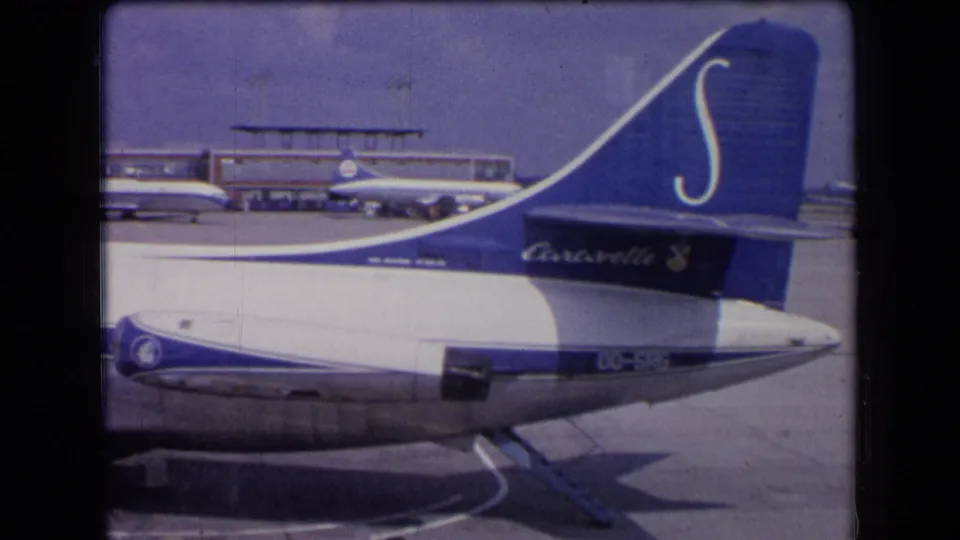 A Sabena tail section dominates the frame at the airport, showing blue livery, rear fuselage, wing, tarmac, and distant aircraft.