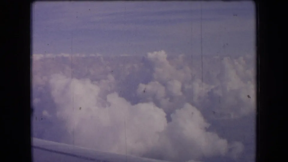 1963 France 8mm frame showing a passenger-window view over clouds, with a partial airplane wing along the bottom edge.