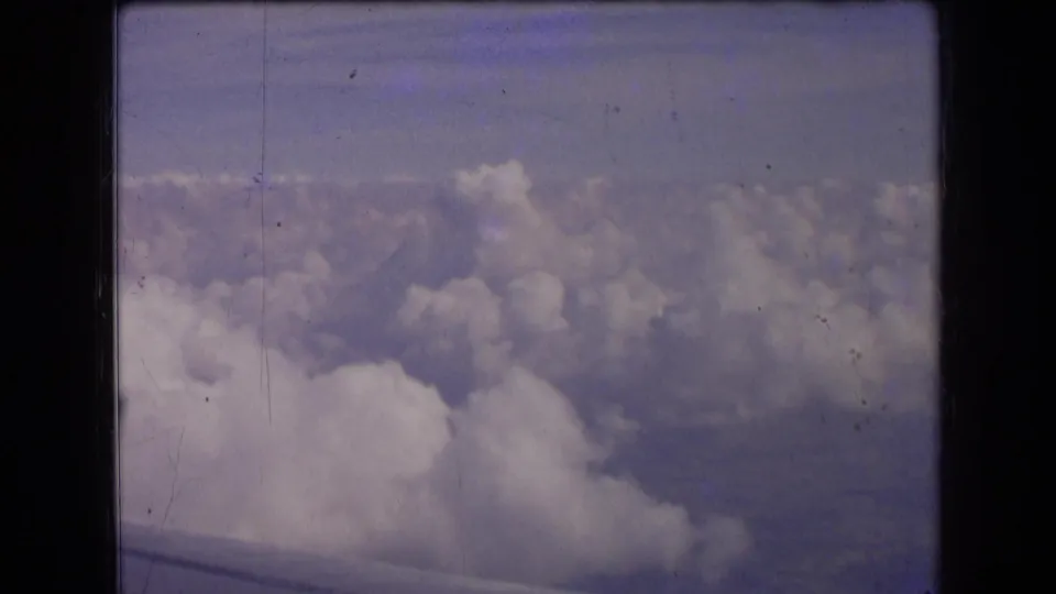 1963 in-flight home-movie frame with a large cloud mass below and the plane wing crossing the lower edge.