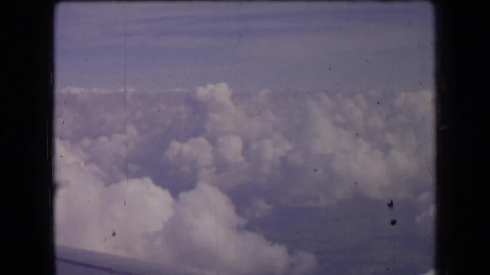 Passenger-window view over cloud tops in 1963 France footage, with faint ground or shadow detail beyond the clouds.