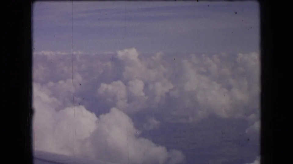 1963 France 8mm frame showing a high aerial view over white clouds with faint land visible beneath a blue-purple sky.