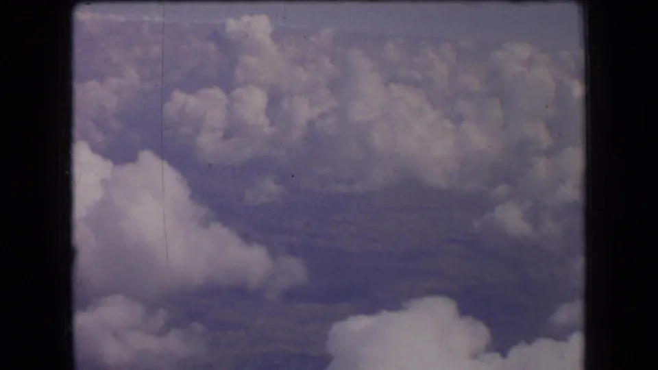 1963 France 8mm frame showing a bright foreground cloud and scattered clouds over hazy terrain below.