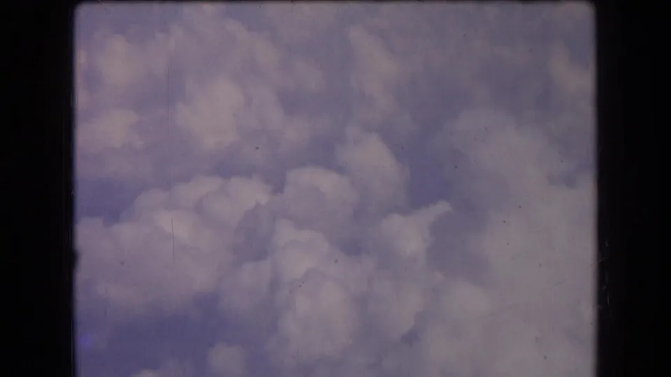1963 8mm home-movie frame from France showing soft white clouds drifting across a muted blue sky with light grain and dust.