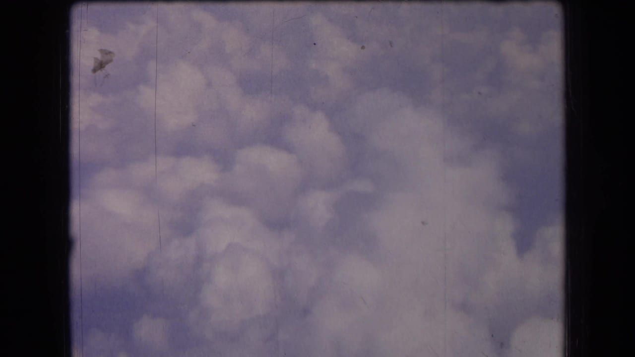 1963 France 8mm frame with billowing clouds against pale blue sky, visible dust, scratches, and dark film border edges.