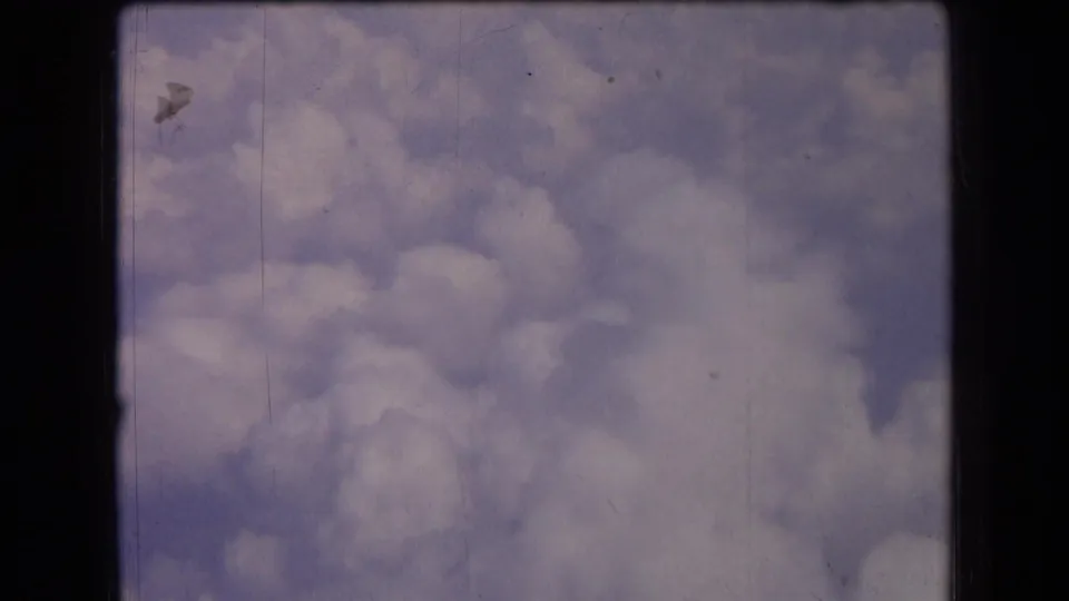 1963 France 8mm frame with billowing clouds against pale blue sky, visible dust, scratches, and dark film border edges.