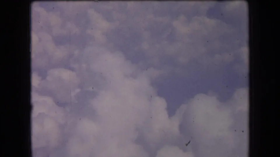 Archival 8mm frame from 1963 France showing soft clouds and a muted blue sky opening, with dust specks and contact-sheet edges.