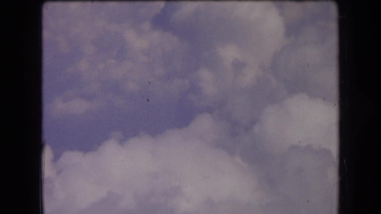 1963 France 8mm sky view with billowing clouds, muted color, light grain, and dark scan borders around the frame.