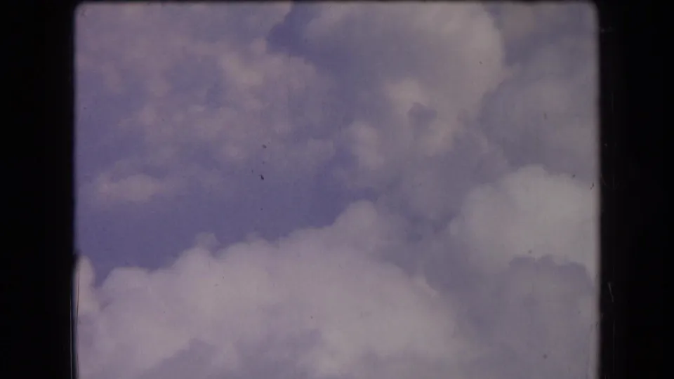 1963 France 8mm sky view with billowing clouds, muted color, light grain, and dark scan borders around the frame.