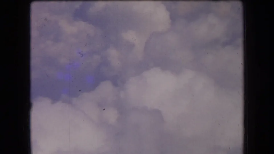 1963 France 8mm frame with layered pale clouds, darker gray cloud patches, faded color, and visible film texture.