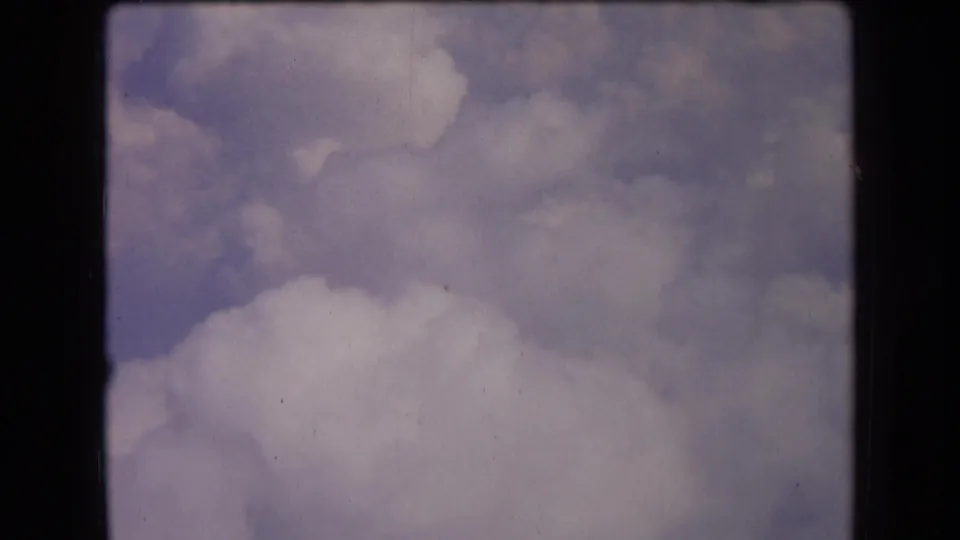 1963 France 8mm sky frame showing a dense white cloud mass below softer gray clouds, with faded color and visible grain.