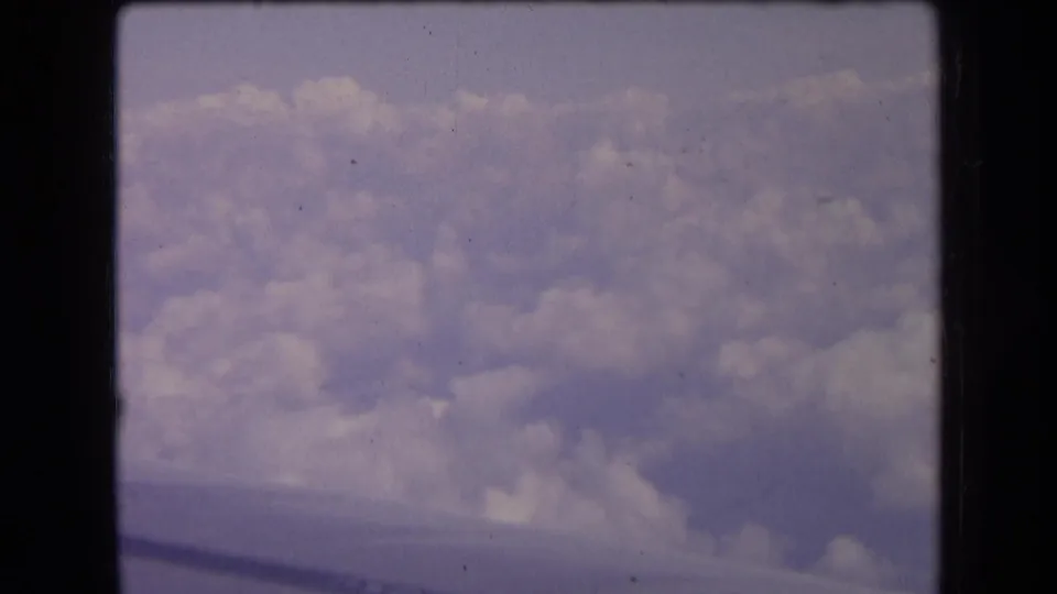 8mm frame from a 1963 France travel clip showing soft clouds below the aircraft and a dark wing edge near the bottom.