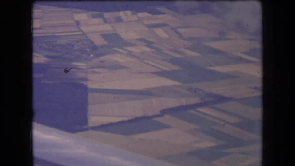 Final 8mm frame from an airplane over rural France, with the wing edge below and patchwork fields and wooded land visible through faded color.