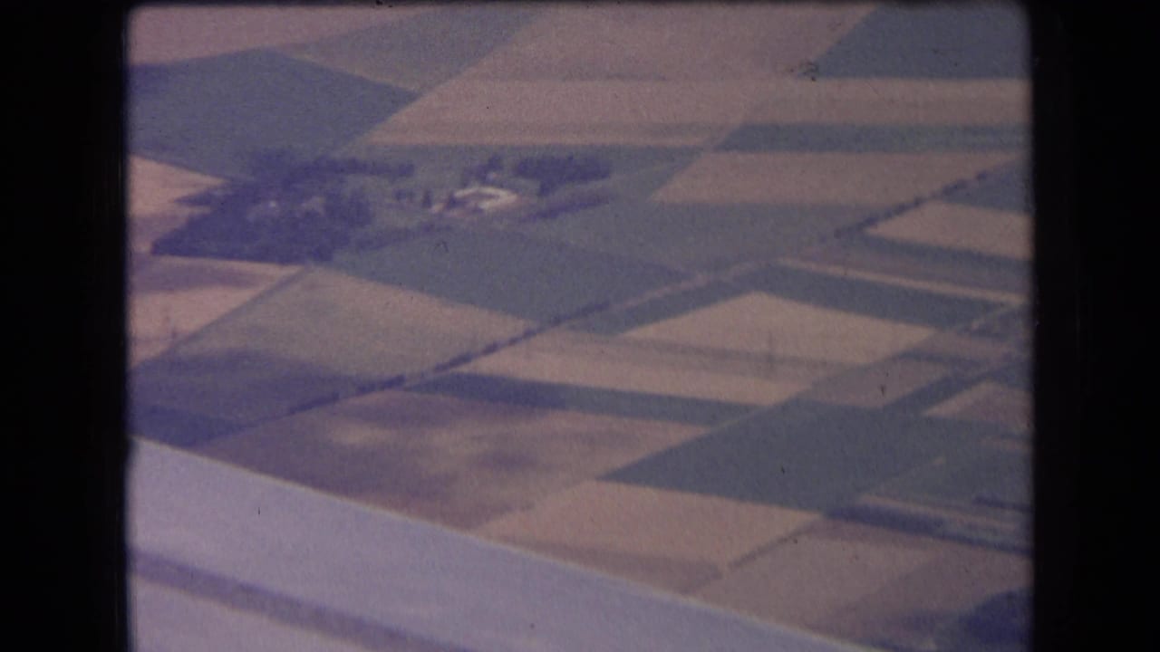 Soft aerial view of patchwork farm fields with scattered buildings and trees.