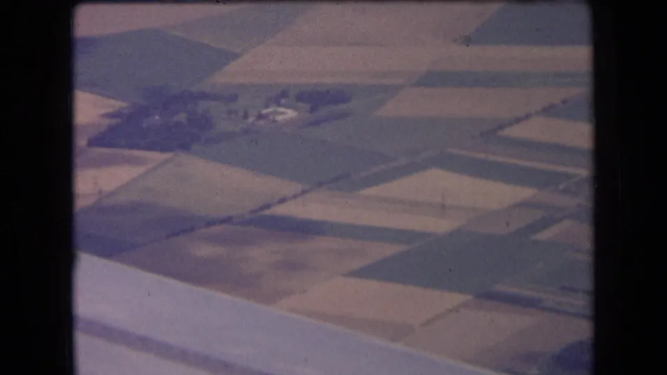1963 8mm aerial view over central France farmland, showing rectangular fields, tree clusters, and small farm buildings.