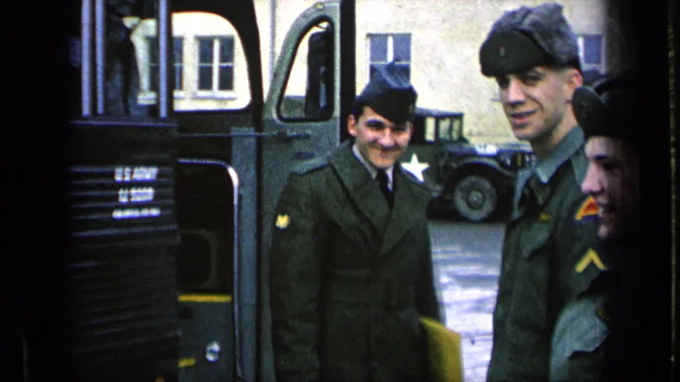 On a Germany military base in 1963, U.S. Army soldiers stand near a bus while another star-marked vehicle is parked behind them.