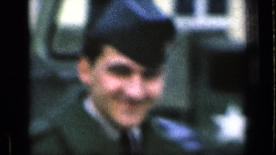 A soft-focus 8mm close-up shows the smiling soldier near military vehicles on the Germany base.