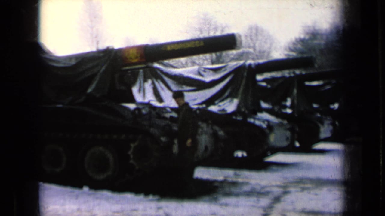 Covered tank with gun barrel and a uniformed man standing beside it.