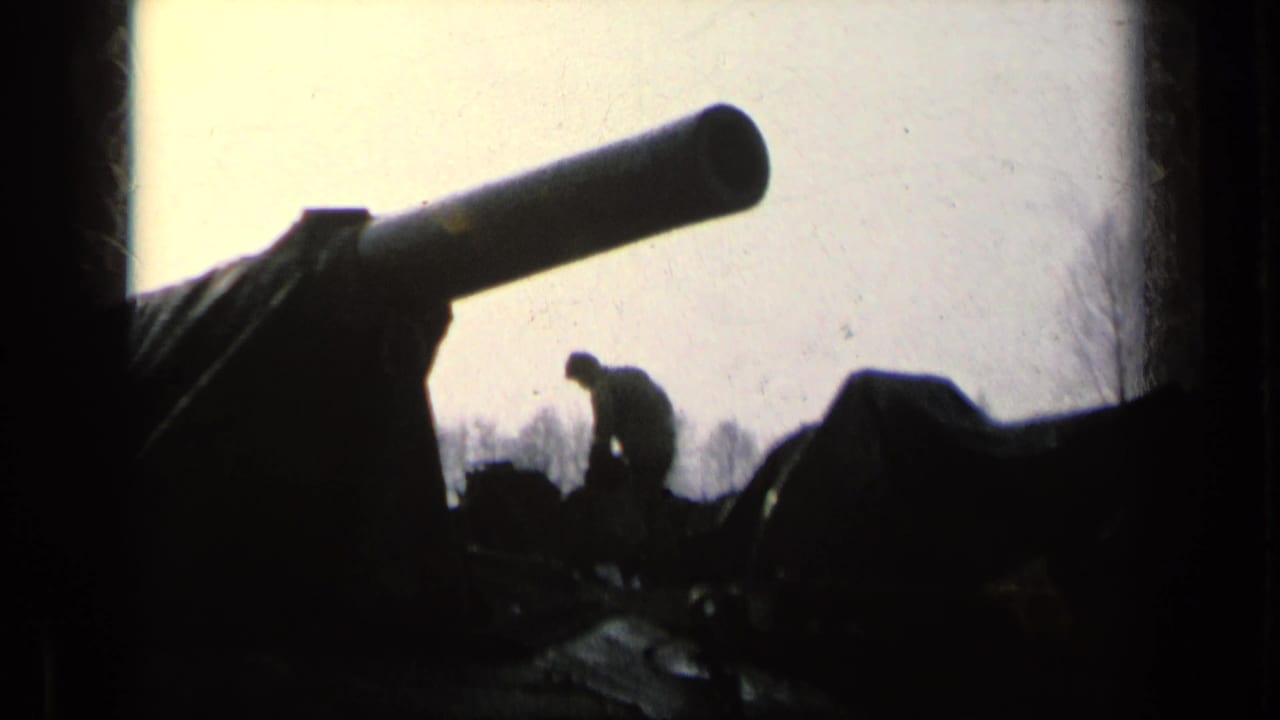 Silhouetted soldier near a tank gun and covered armored vehicle.