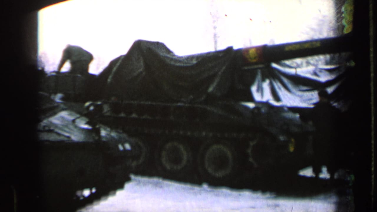 Snowy row of covered military tanks with a person near the left edge.