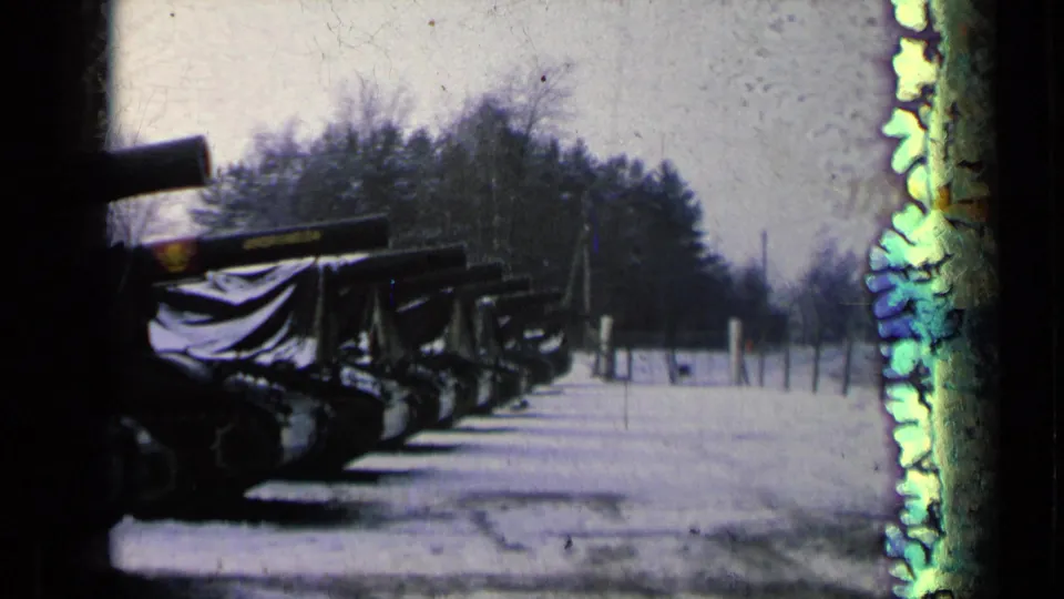 8mm frame of covered military tanks parked in snow, with trees behind them and bright edge damage on the film.