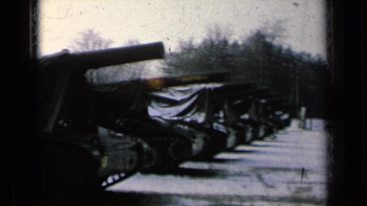 Row of tarp-covered tanks with gun barrels on snow-dusted ground.