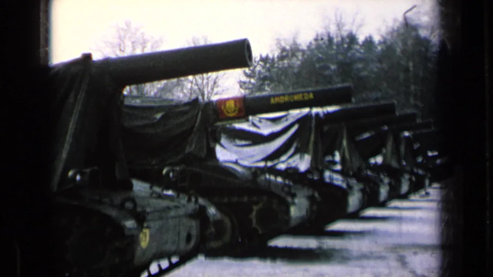 Closer 8mm frame of tarp-covered tanks in a row, with ANDROMEDA visible on a gun barrel.