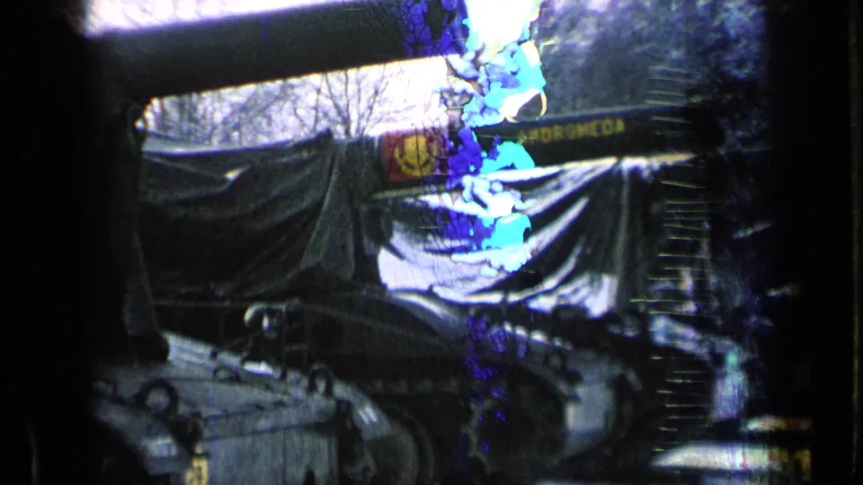 Close 1963 8mm view of a tarp-covered tank and barrel, with blue film artifacting across the frame.