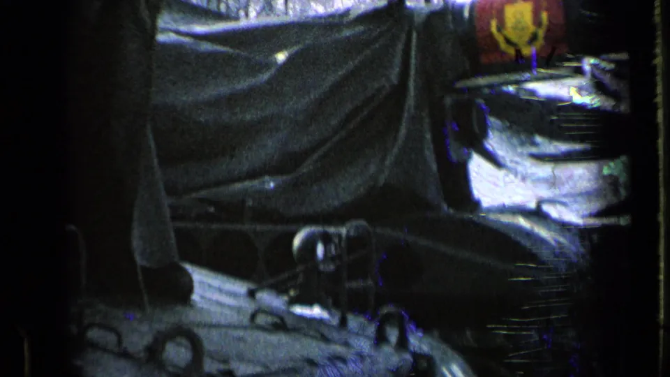 Close 8mm frame of a covered armored vehicle with tarps, metal fittings, and snow visible around the base.