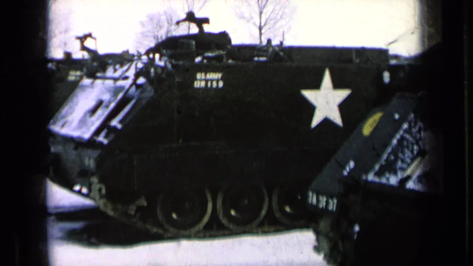 1963 8mm frame showing a U.S. Army tracked armored vehicle with a white star and stenciled markings parked on pale ground.